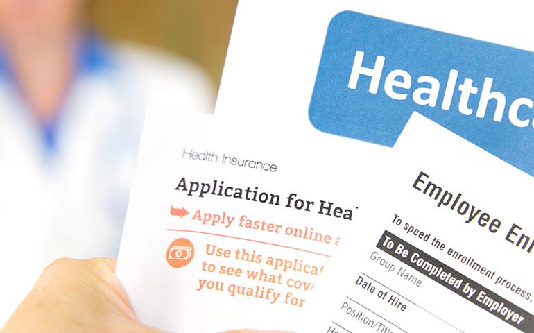 Stock image of a hand holding different enrollment and healthcare forms.
