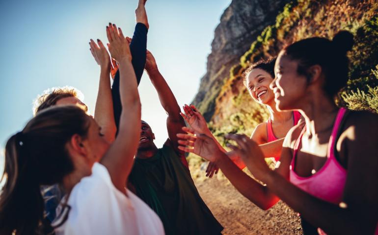 Photo of a group of women cheering and giving high fives outside on a trail.
