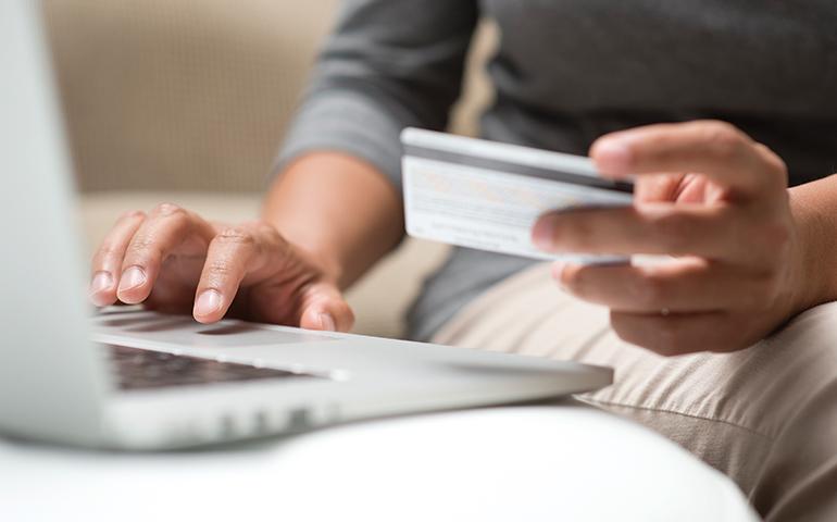 Seated man holding a credit card in front of a laptop.