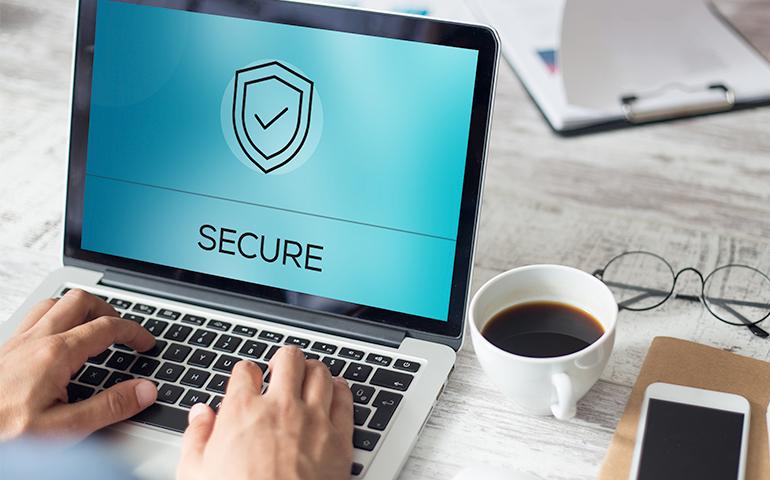 Photo of man's hands typing on a laptop computer with an image of a shield on the screen denoting security.