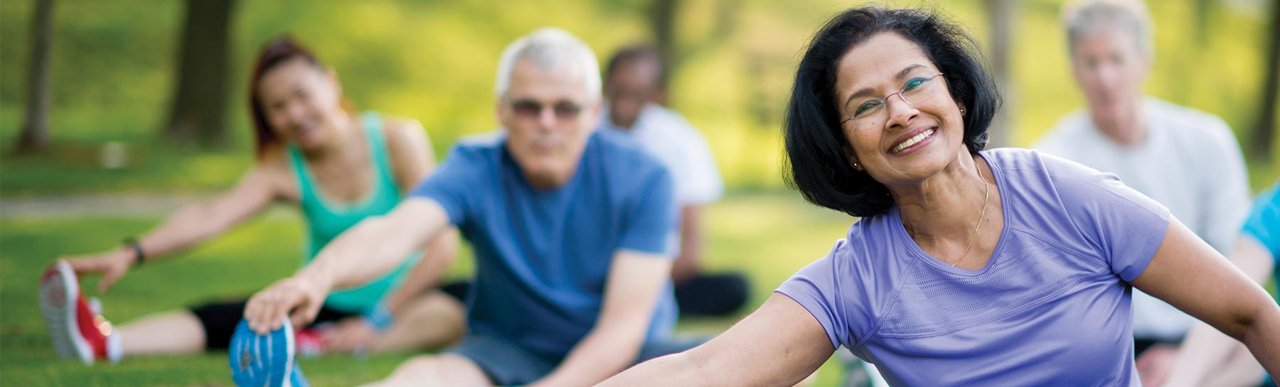 Image of older adults sitting outside stretching on exercise mats.