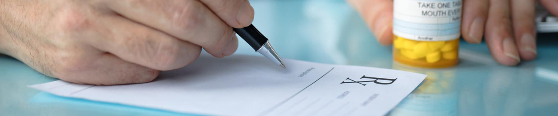 An image of a doctor writing on a perscrition pad and a bottle of perscription on a table. 