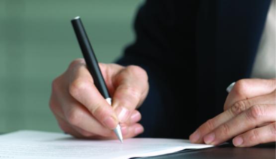 Photo of a woman's hand writing on a pad with a black pen.