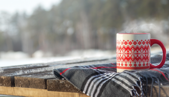 A cup with a festive design behind a snow landscape background with trees.